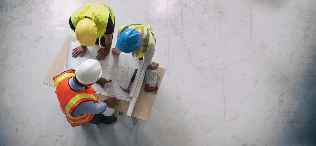 Birds eye view of three engineers reviewing a blue print